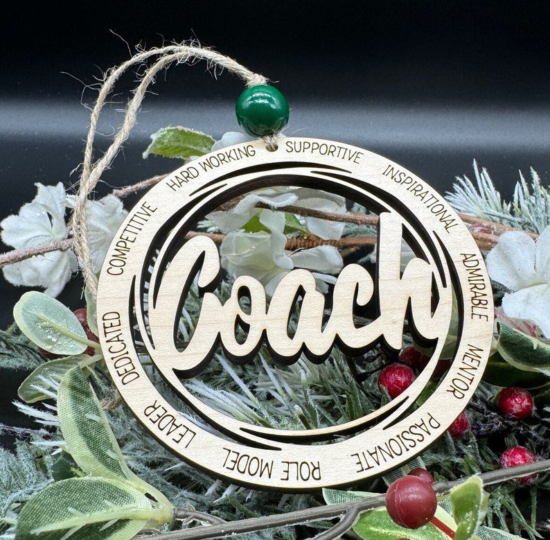 May include: Wooden ornament with the word "Coach" in a decorative font. The ornament is surrounded by a circle with the words "Hard Working", "Supportive", "Inspirational", "Admirable", "Mentor", "Passionate", "Role Model", "Leader", "Dedicated", "Competitive" inscribed around the circle.