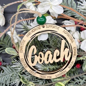 May include: Wooden ornament with the word "Coach" in a circle with the words "Hard Working", "Supportive", "Inspirational", "Admirable", "Mentor", "Passionate", "Role Model", "Leader", "Dedicated", and "Competitive" around the circle.