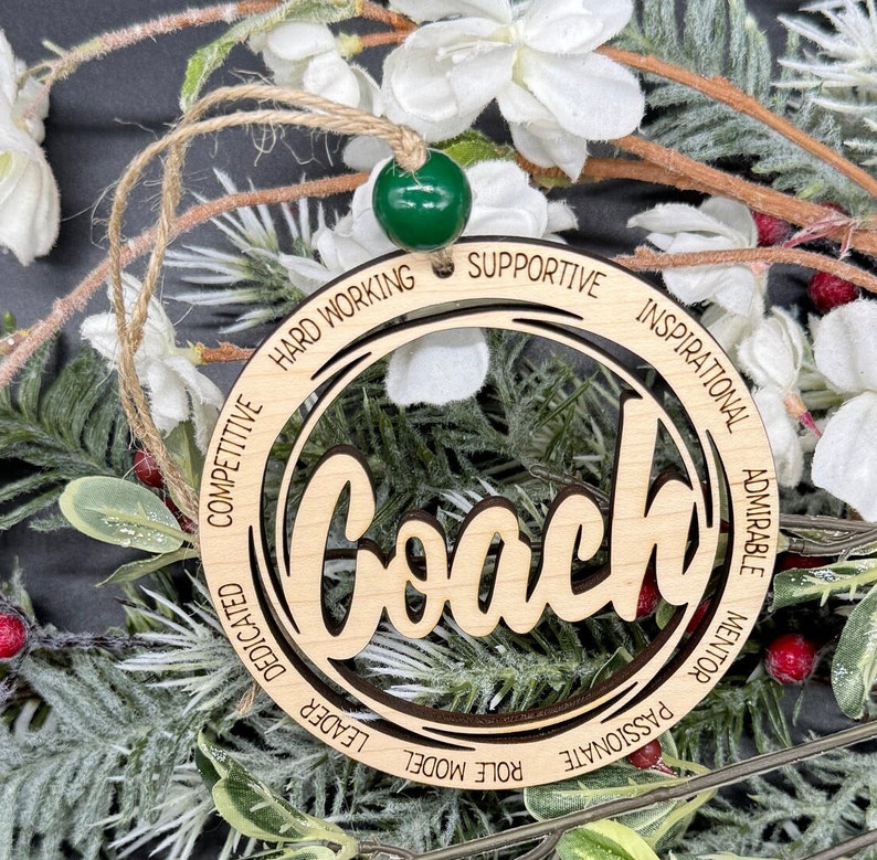 May include: Wooden ornament with the word "Coach" in a circle with the words "Hard Working", "Supportive", "Inspirational", "Admirable", "Mentor", "Passionate", "Role Model", "Leader", "Dedicated", and "Competitive" around the circle.