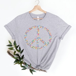 May include: A heather gray t-shirt with a peace sign made of colorful leaves. The peace sign is centered on the shirt.