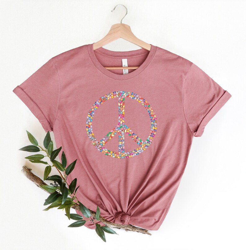 May include: A mauve t-shirt with a peace sign made of colorful beads.
