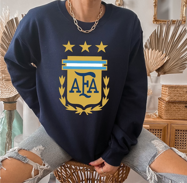 May include: A navy blue sweatshirt with a gold crest featuring three stars, a blue and white stripe, and the letters "AFA".