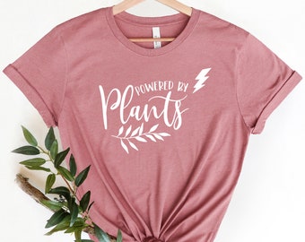 May include: A mauve t-shirt with a white graphic that says "Powered by Plants" with a lightning bolt and a small branch with leaves.