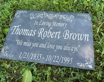 May include: A black slate memorial plaque with white floral designs and the inscription "In Loving Memory Thomas Robert Brown "We miss you and love you always" 1/23/1935 - 10/22/1995"