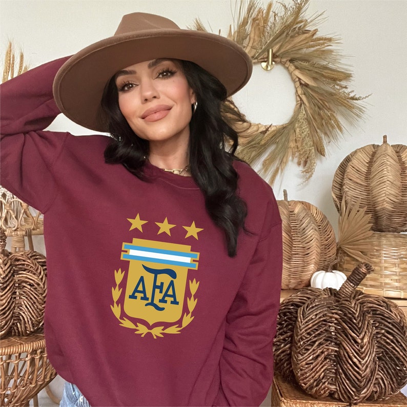 May include: A maroon sweatshirt with a gold and blue crest featuring three stars, a blue and white stripe, and the letters "AFA".