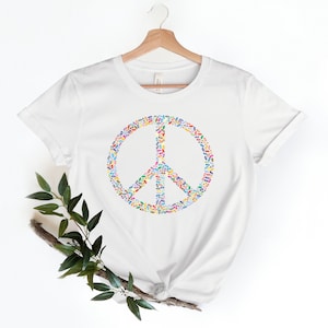 May include: White t-shirt with a peace sign made of colorful leaves.