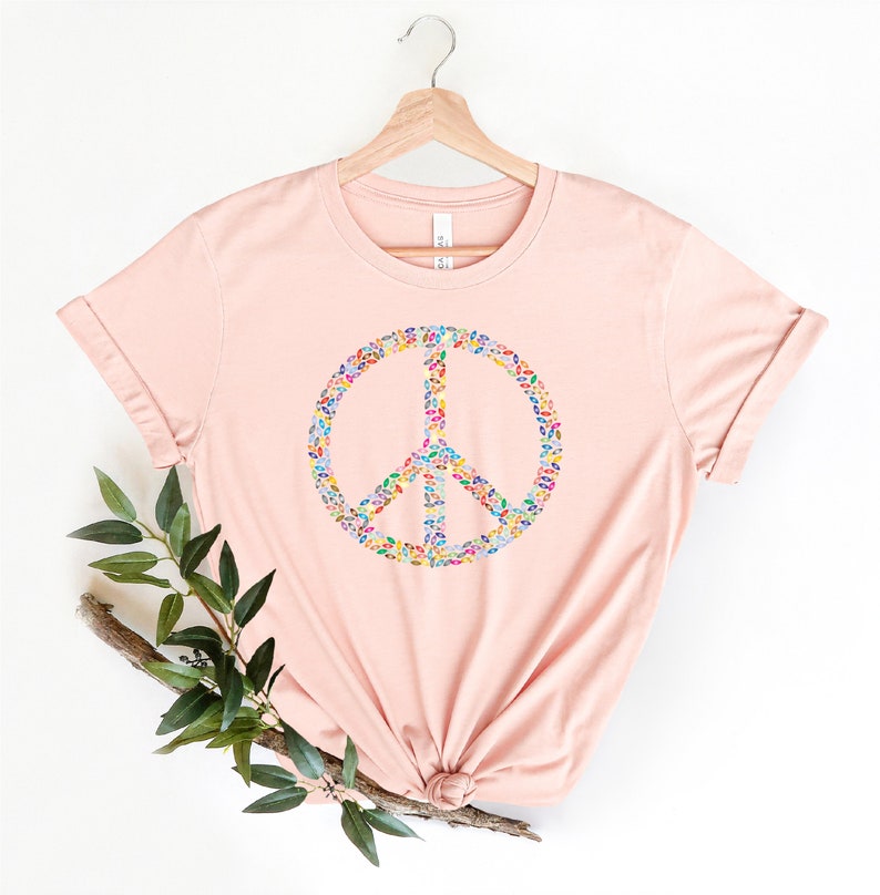 May include: A pink t-shirt with a peace sign made of colorful leaves. The peace sign is centered on the shirt.