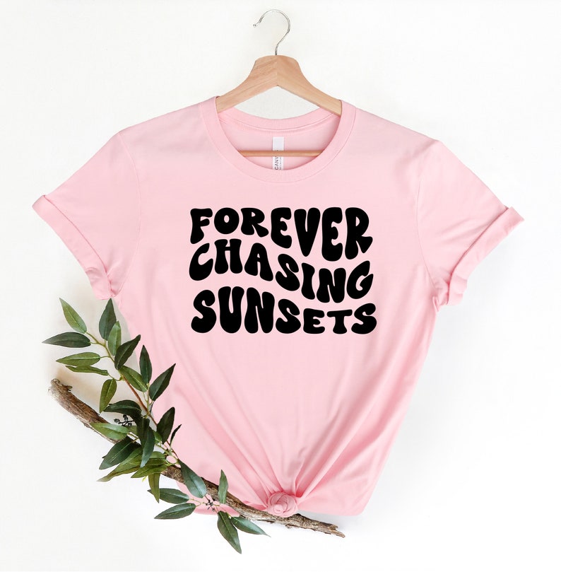 May include: Pink t-shirt with the text "FOREVER CHASING SUNSETS" in black, retro-style lettering.