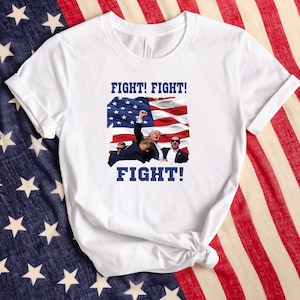 May include: White t-shirt with a blue and red American flag graphic and the text "FIGHT! FIGHT! FIGHT!" printed on it.
