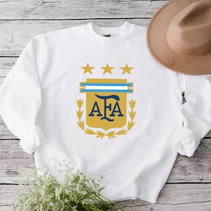 May include: White sweatshirt with a gold and blue crest featuring the letters "AFA" and three stars.