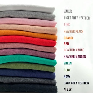 May include: A stack of folded fabric swatches in various colors, including white, light grey heather, pink, heather peach, orange, red, heather mauve, heather maroon, green, olive, navy, dark grey heather, and black. The colors are labeled on the right side of the image.