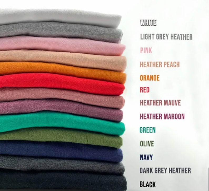 May include: A stack of folded fabric swatches in various colors, including white, light grey heather, pink, heather peach, orange, red, heather mauve, heather maroon, green, olive, navy, dark grey heather, and black. The colors are labeled on the right side of the image.