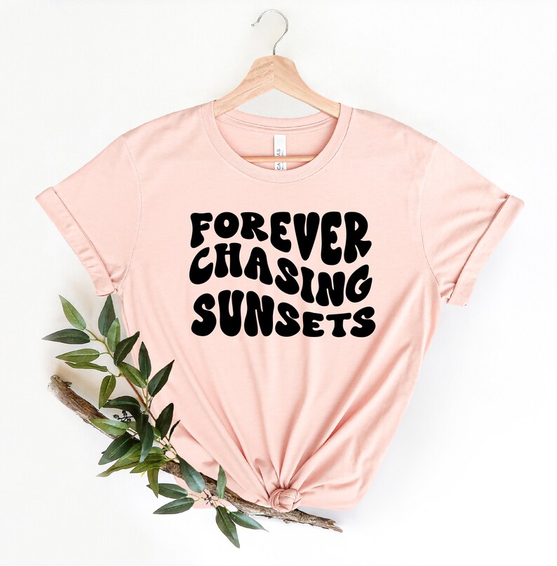 May include: A pink t-shirt with the text "FOREVER CHASING SUNSETS" in black, retro-style lettering.