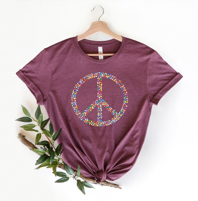 May include: A maroon t-shirt with a peace sign made of colorful leaves. The peace sign is centered on the shirt.