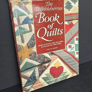 May include: A Rodale quilt book titled "The Thimbleberries Book of Quilts" with a red cover and colorful quilt patterns. The book features decorative accessories and projects for quilting. The cover has the author's name, Lynette Jensen.