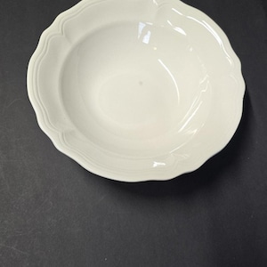 May include: A white ceramic bowl with a scalloped rim. The bowl has a shallow, rounded interior and a smooth, glossy finish. The bowl is likely for serving soups, salads, or other dishes.
