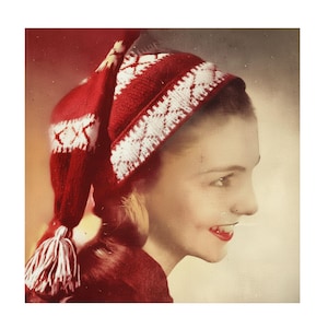 May include: A vintage photograph shows a person wearing a red knitted hat with white geometric patterns. The hat has a tassel and is paired with a red garment. The person is smiling, with red lipstick.
