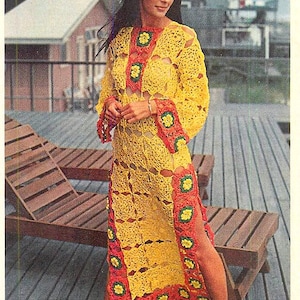 May include: A long, open-weave crochet dress in yellow, with red and green floral accents. The dress features long sleeves and a high slit on one side. The dress is worn outdoors near wooden lounge chairs.