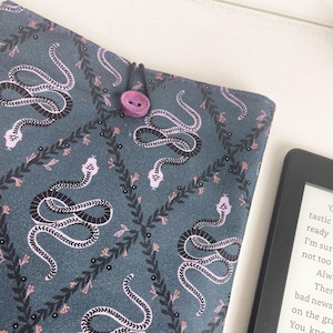 May include: A teal blue fabric book cover with a repeating pattern of black and pink snakes and vines. A pink button is attached to the cover with a black string.