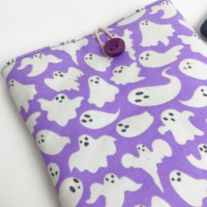 May include: Purple fabric with a white ghost pattern. The fabric has a button and a loop for attaching a strap.