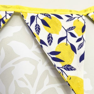 May include: A white fabric bunting with yellow lemons and navy blue leaves. The bunting has a yellow trim and is sewn together with white thread.