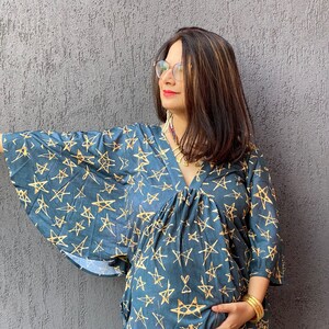 Può includere: Abito scollato a V color teal con motivo a stelle dorate. L'abito presenta maniche ampie e vita arricciata. Il tessuto appare morbido e fluido, adatto per un abbigliamento casual. È un abito premaman.