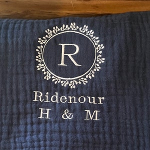 Puede incluir: Una almohada azul oscuro con bordado blanco. El bordado presenta una corona con la letra "R" en el centro y el texto "Ridenour H & M".