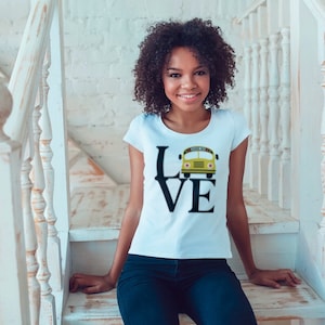 Puede incluir: Una camiseta blanca con un gr&aacute;fico negro de la palabra "LOVE" con un autob&uacute;s escolar amarillo reemplazando la "O".