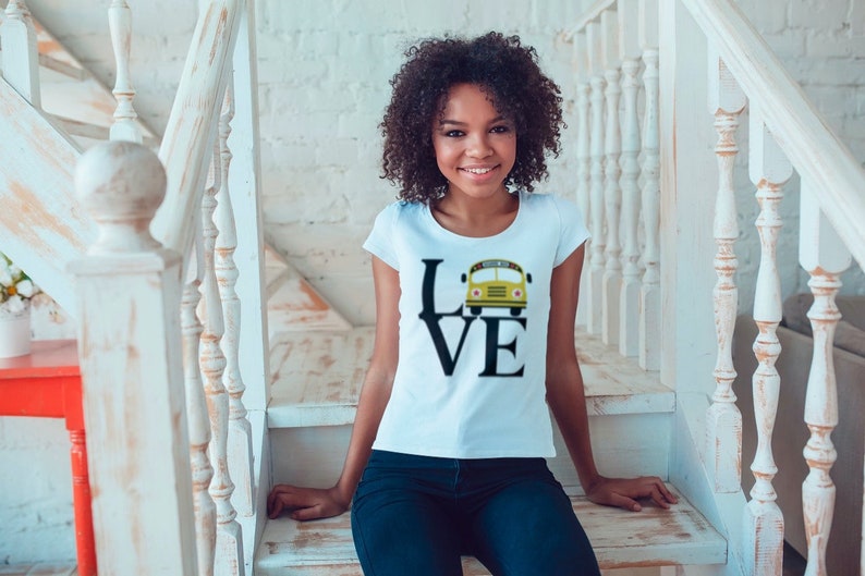 Puede incluir: Una camiseta blanca con un gr&aacute;fico negro de la palabra "LOVE" con un autob&uacute;s escolar amarillo reemplazando la "O".