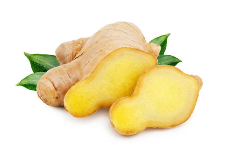 May include: A close-up of a ginger root with two slices, showing the light yellow flesh. The ginger root is surrounded by green leaves.