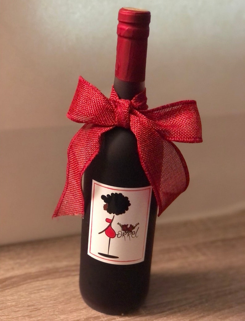 May include: A red wine bottle with a red bow and a label featuring a black woman with a red dress and the word "orrel".
