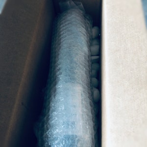 May include: A brown cardboard box with a white bubble wrap package inside. The package is secured with white packing peanuts.