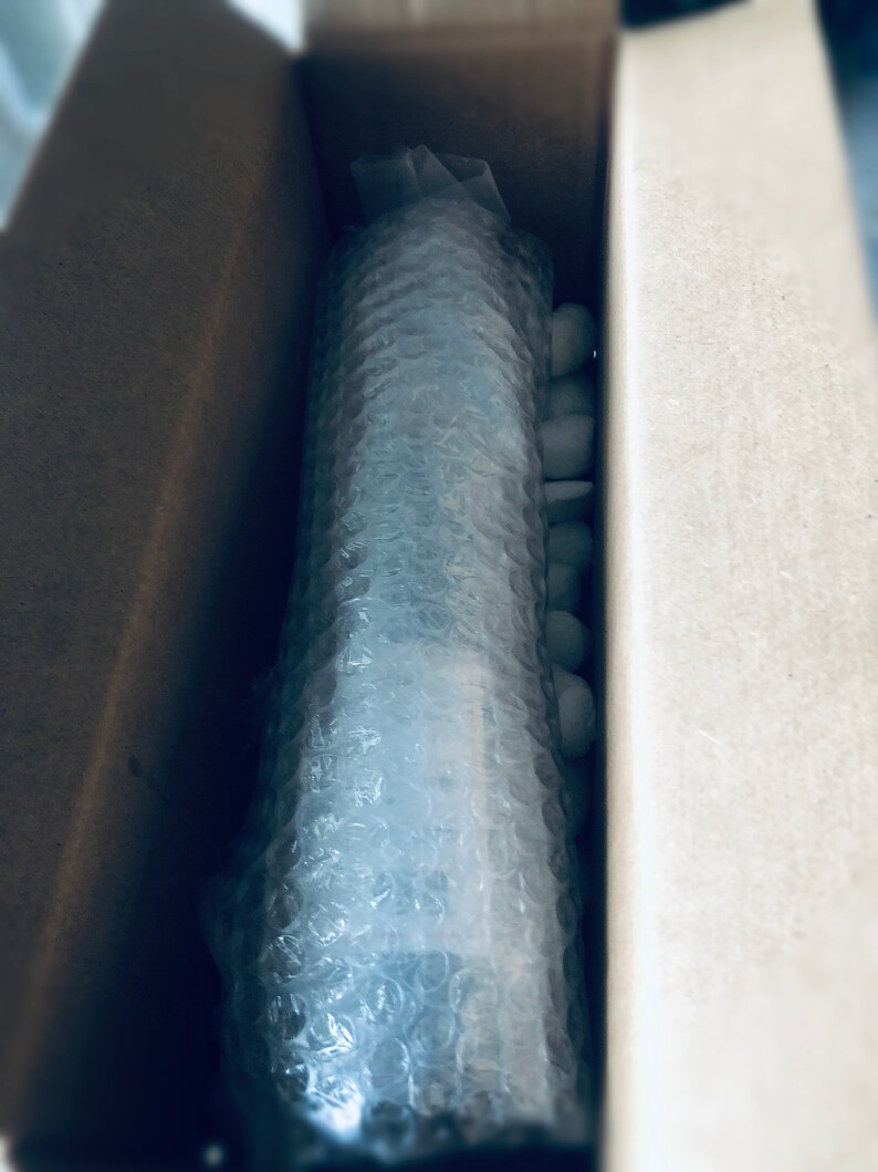 May include: A brown cardboard box with a white bubble wrap package inside. The package is secured with white packing peanuts.