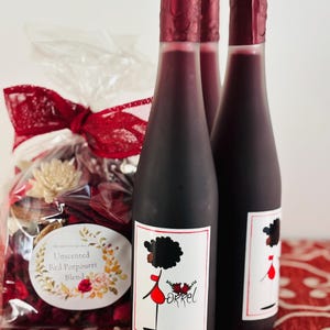 May include: Three glass bottles of red wine with a black and white label featuring a cartoon woman in a red dress. The label also includes the word "Orrel".