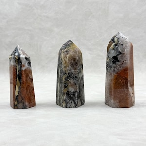 Puede incluir: Tres obeliscos de piedra pulida. Los obeliscos tienen una mezcla de colores, incluyendo rojo, marr&oacute;n, negro y blanco. Cada obelisco tiene una parte superior puntiaguda y una base rectangular. Las piedras tienen un aspecto natural y texturizado.