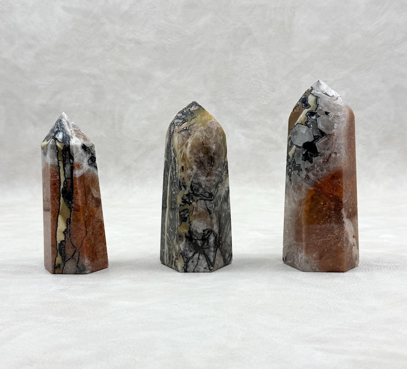 Puede incluir: Tres obeliscos de piedra pulida. Los obeliscos tienen una mezcla de colores, incluyendo rojo, marr&oacute;n, negro y blanco. Cada obelisco tiene una parte superior puntiaguda y una base rectangular. Las piedras tienen un aspecto natural y texturizado.