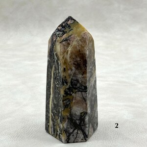 Puede incluir: Un obelisco de piedra hexagonal con una parte superior puntiaguda. La piedra presenta una mezcla de colores, incluyendo negro, marr&oacute;n, amarillo y rosa, con intrincados patrones y vetas. El obelisco es un art&iacute;culo decorativo.