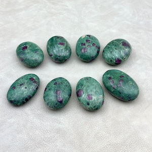 May include: Eight smooth, oval-shaped green stones with red ruby inclusions. The stones are tumbled and polished, and they have a natural, organic look.