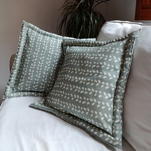 Puede incluir: Dos almohadas verdes para sofá con un patrón abstracto blanco. Las almohadas están en un sofá blanco.