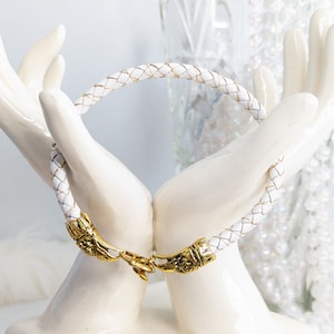 May include: White leather bracelet with a gold clasp and woven design.
