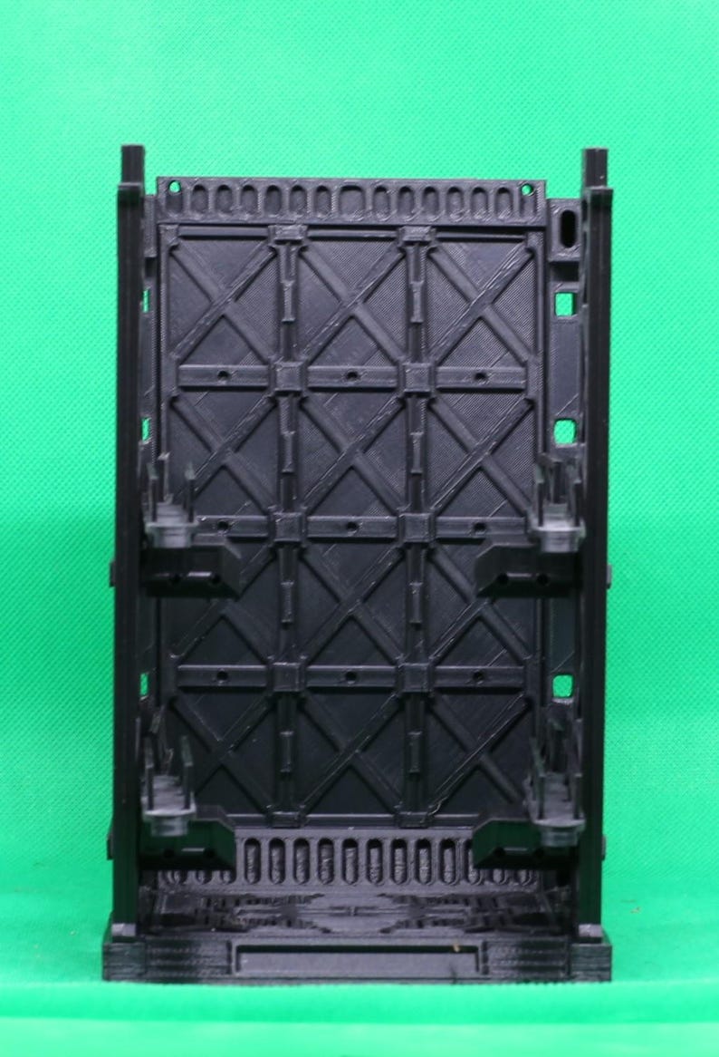 May include: A black plastic structure with a geometric design. The structure has a rectangular shape with a grid-like pattern of intersecting lines and square details. It features vertical supports and a base, likely for display or support.