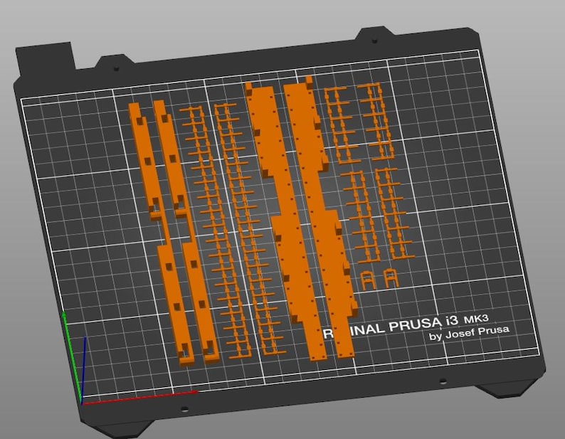 Peut inclure: Un plateau d'impression 3D avec une disposition d'impression orange. La disposition comprend diverses formes rectangulaires et lin&eacute;aires. Le texte "ORIGINAL PRUSA i3 MK3 by Josef Prusa" est visible.