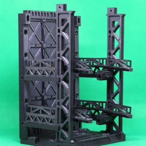 May include: A black, 3D-printed model of a futuristic industrial structure. The model features a complex network of support beams, platforms, and a large, closed door. The design suggests a sci-fi or architectural theme.