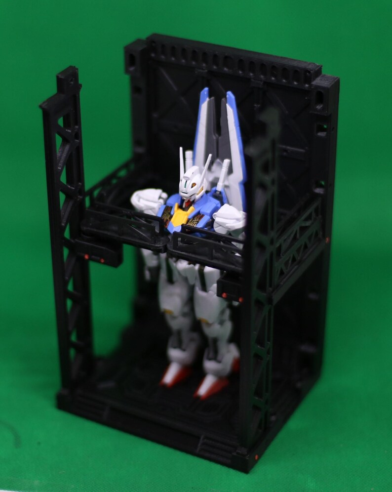 May include: A detailed robot model in white, blue, and yellow is positioned within a black geometric structure. The robot features red feet and white armour. The structure has a cage-like design with support beams and a platform.