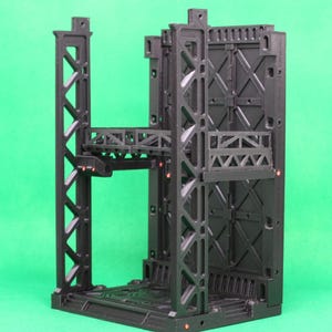 May include: A black, modular, industrial-themed structure with multiple levels and intricate geometric designs. The structure features support beams, platforms, and a textured surface, suitable for miniature gaming or display.