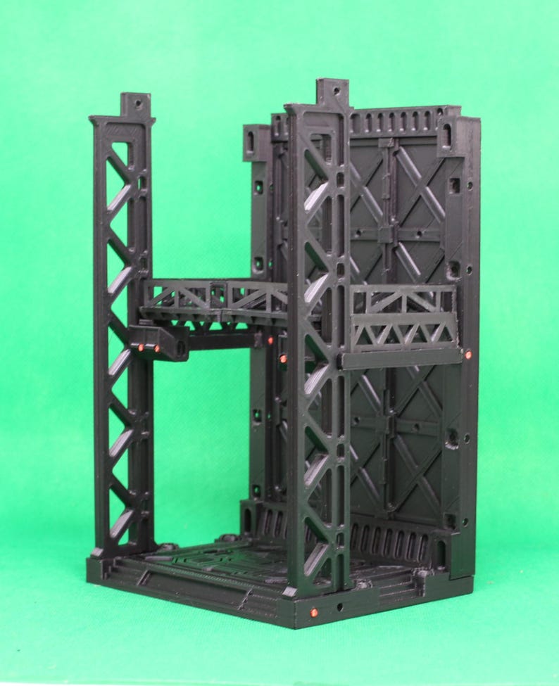 May include: A black, modular, industrial-themed structure with multiple levels and intricate geometric designs. The structure features support beams, platforms, and a textured surface, suitable for miniature gaming or display.