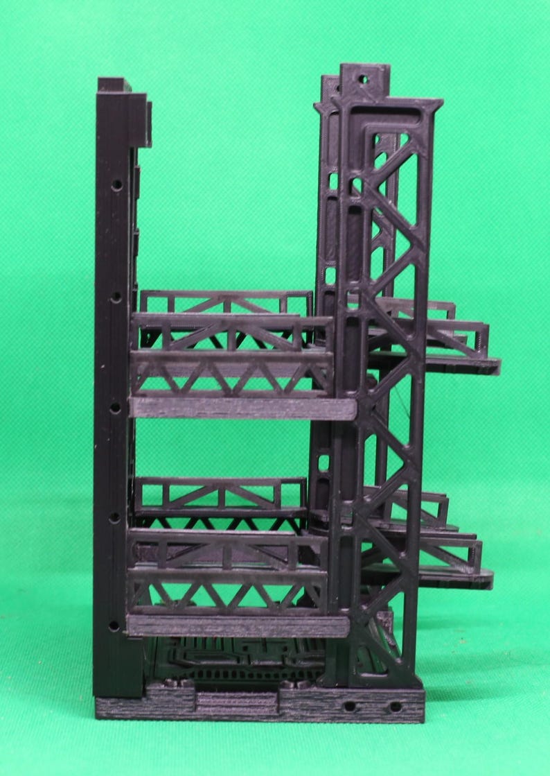 May include: A black, 3D-printed architectural model with multiple levels and a complex, geometric design. The model features a vertical support structure with horizontal platforms and intricate truss-like elements, showcasing a modern aesthetic.