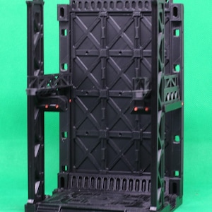 May include: A black, modular sci-fi diorama piece. The structure features a large, textured wall with an X-pattern design, supported by vertical beams and platforms. Small red accents are visible. Designed for tabletop gaming.