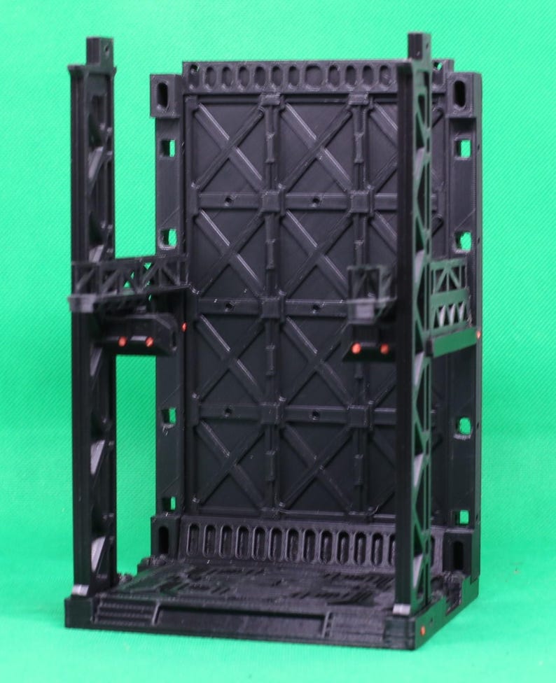 May include: A black, modular sci-fi diorama piece. The structure features a large, textured wall with an X-pattern design, supported by vertical beams and platforms. Small red accents are visible. Designed for tabletop gaming.