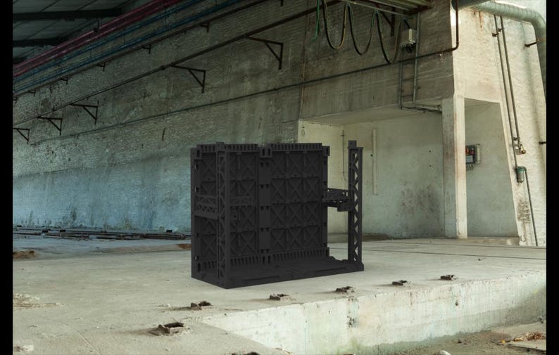 May include: A black, modular building structure with a complex, geometric design. The structure has a series of interconnected panels and a small platform extending from the side. The background is a concrete industrial space.